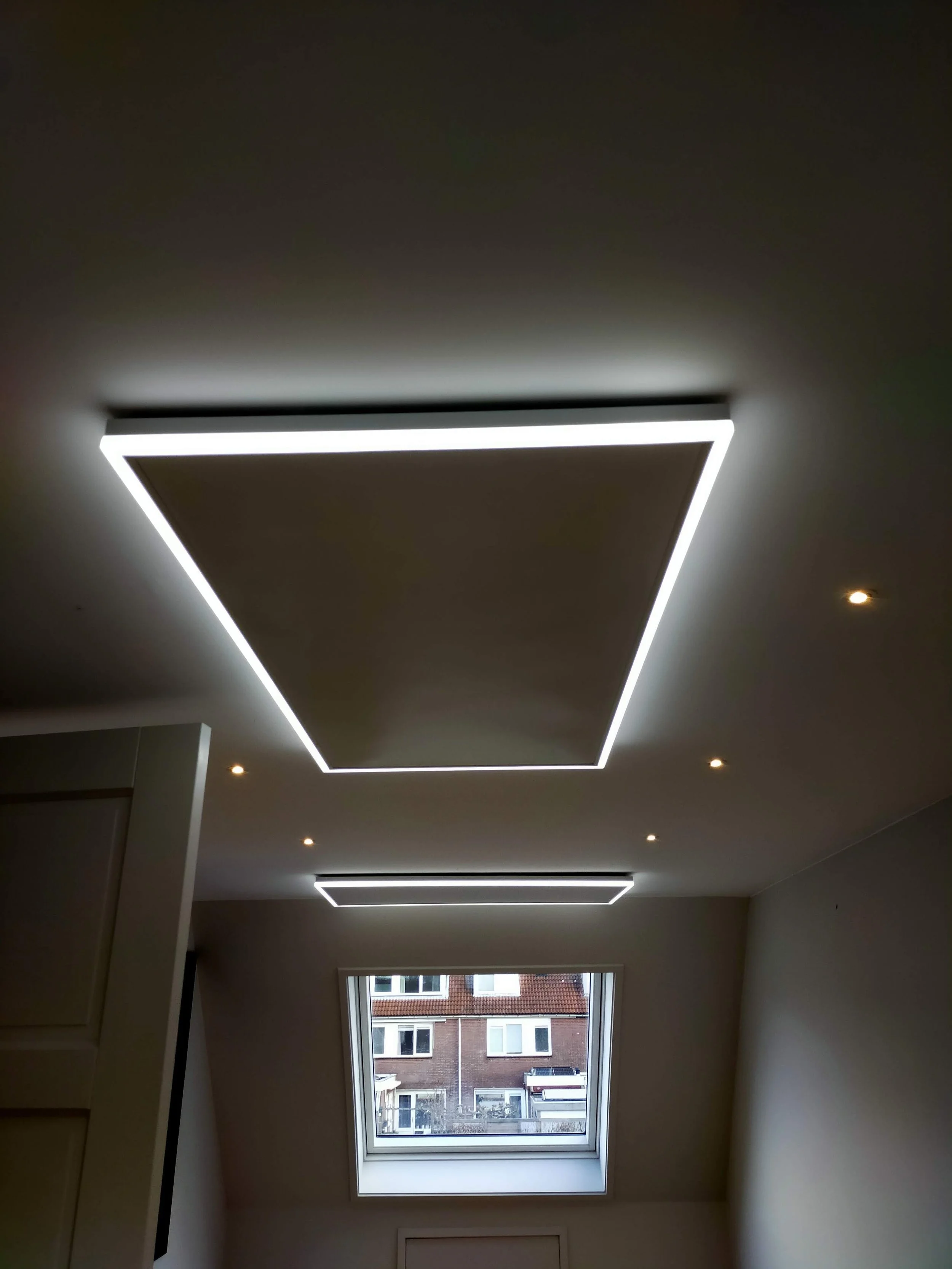 Interior view of a room with a rectangular skylight window, showing a building with brick walls and white-framed windows outside.