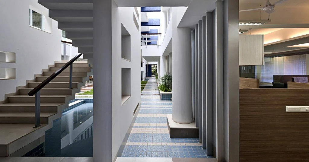 Modern indoor corridor with white walls, blue tiled floor, staircase, and potted plants.