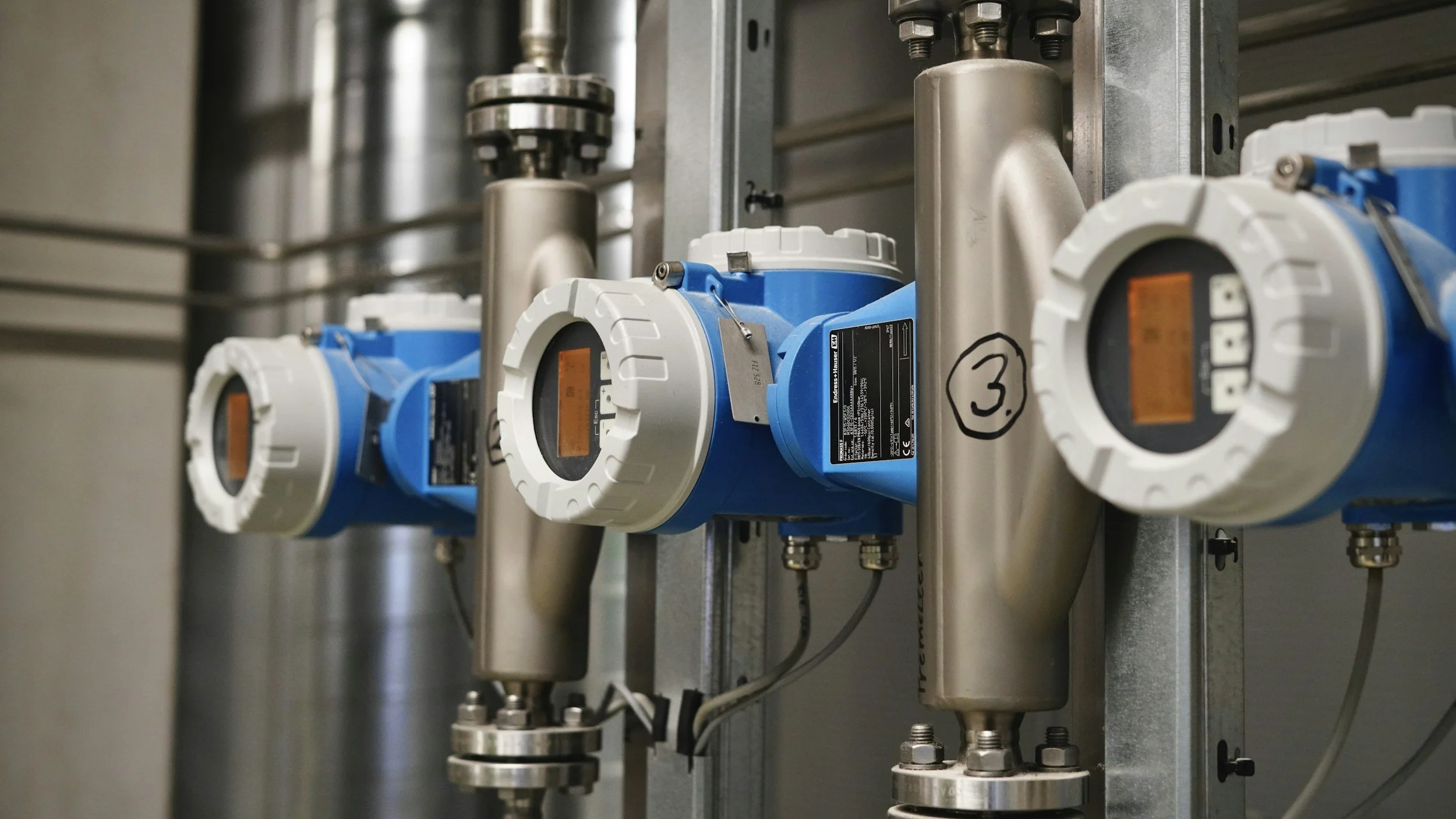 Industrial instrumentation with three blue and white digital valves mounted on metal pipes, in an industrial setting.