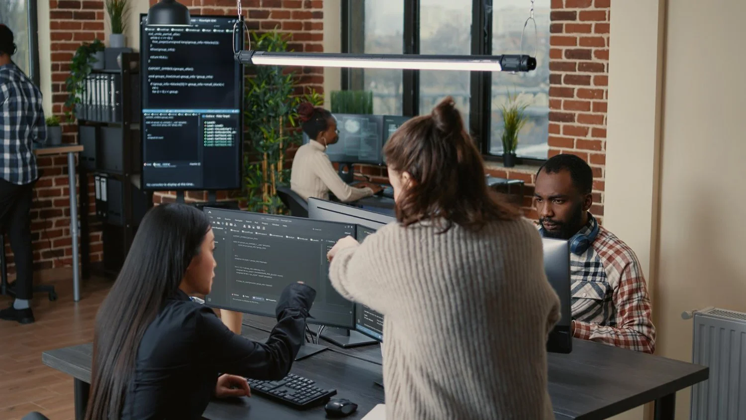 Groupe de personnes travaillant sur des ordinateurs dans un bureau moderne avec murs en briques et grandes fenêtres