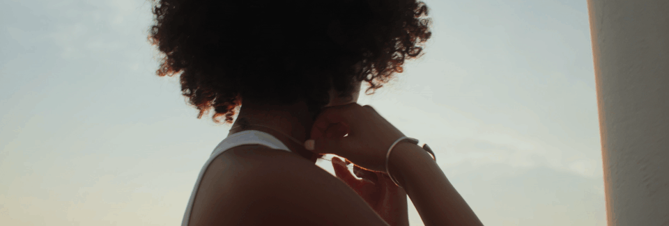 Silhouette of a woman with curly hair looking out at the sky during sunset, touching her face with her hand.