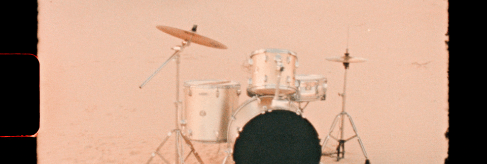 A white drum set with cymbals on stands placed on a light pink background.