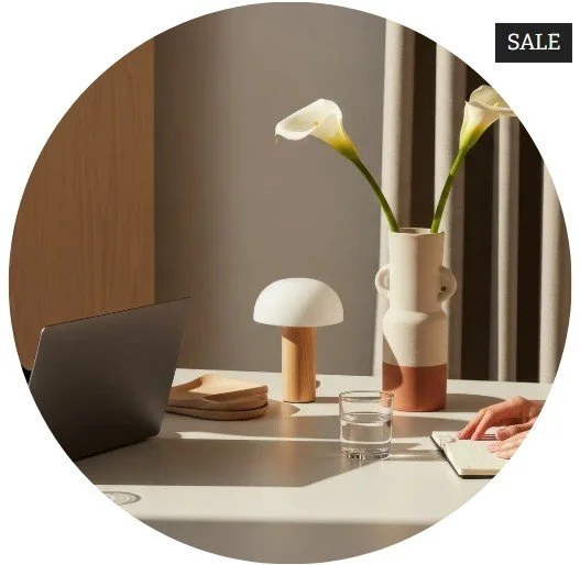A desk with a laptop, a small table lamp, a glass of water, a notebook, and a vase with two white calla lilies. A black sale tag is in the top right corner.