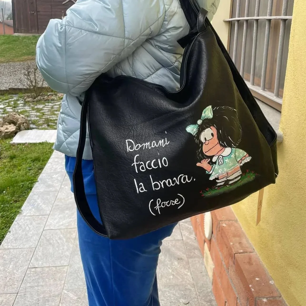 Una borsa di pelle nera con disegno di una bambina e la scritta 'Domani faccio la brava (fouse)'.