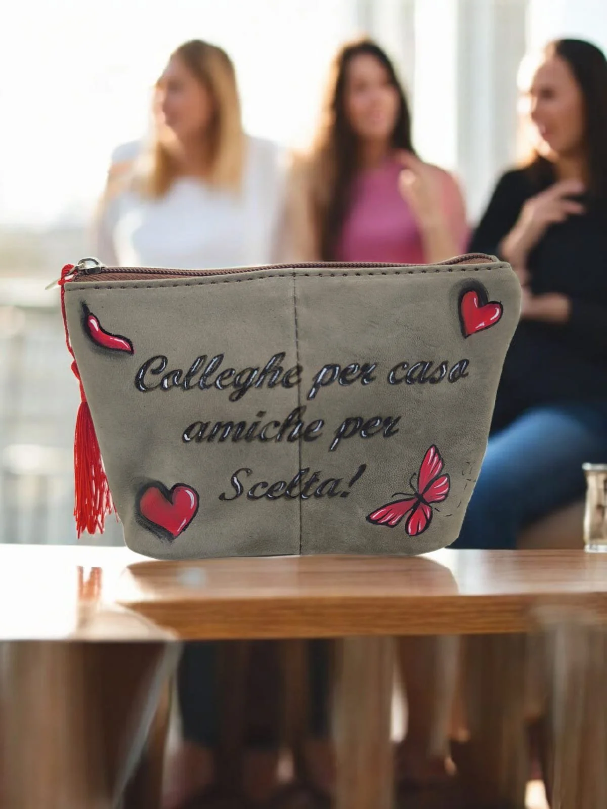 Borsa con scritta in italiano e decorazioni di cuori e farfalle, sullo sfondo tre donne sedute che parlano.
