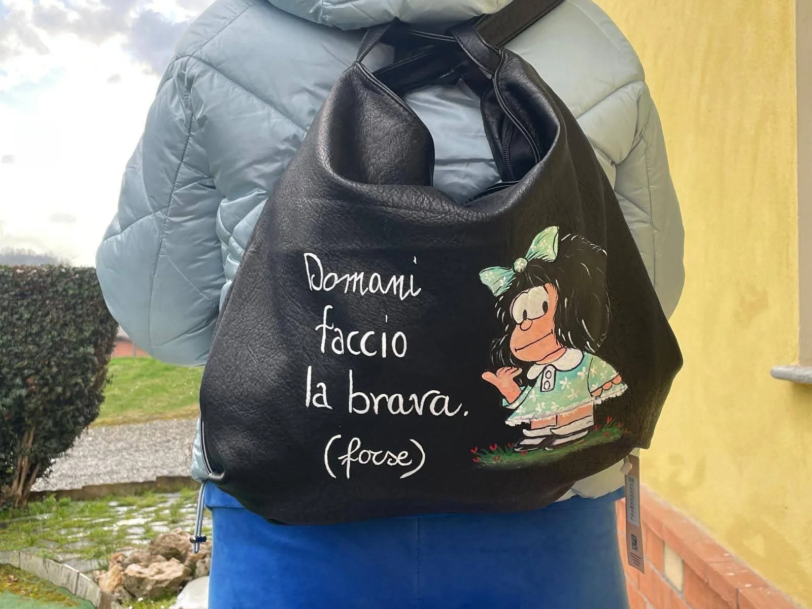 Borsa di cuoio nera con un disegno di una ragazza con grandi occhi, un fiocco in testa, vestita con un abito verde a fiori e la frase 'Domani faccio la brava. (fouse)'