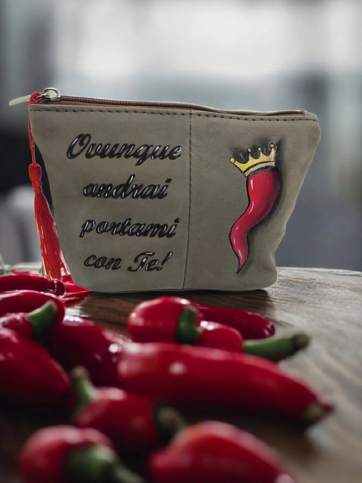 Borsetta beige con scritta in italiano e disegno di un peperoncino con corona. Sul tavolo ci sono dei peperoncini rossi.