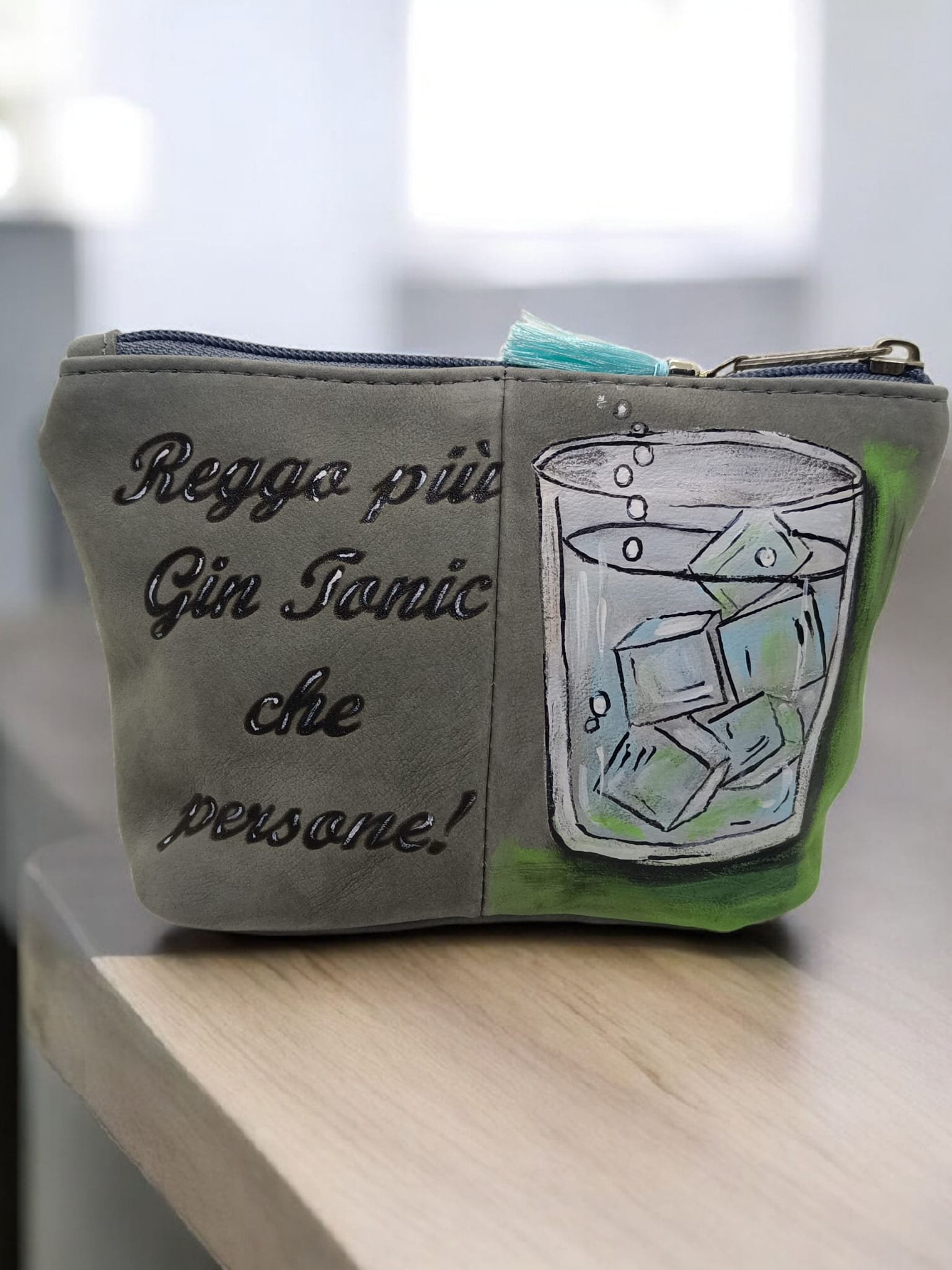 Portamonete decorato con disegni e scritte, raffigurante un bicchiere di gin tonic con limone e ghiaccio, e ha una chiusura con zip blu.