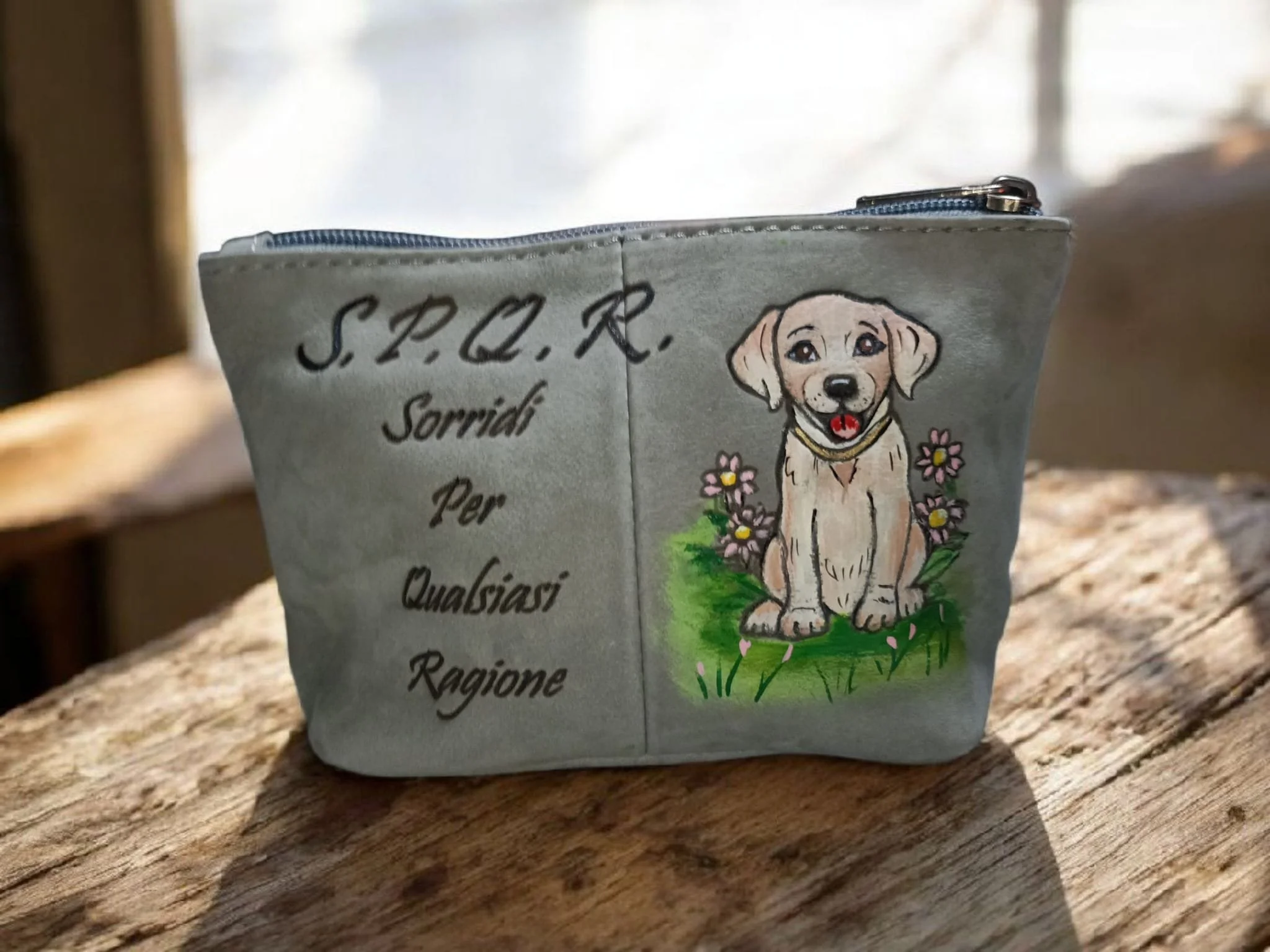 Una borsa di tessuto grigia decorata con un disegno di un cucciolo di cane seduto in un prato con fiori, e con scritte che includono "S.P.R.R." e altre parole.