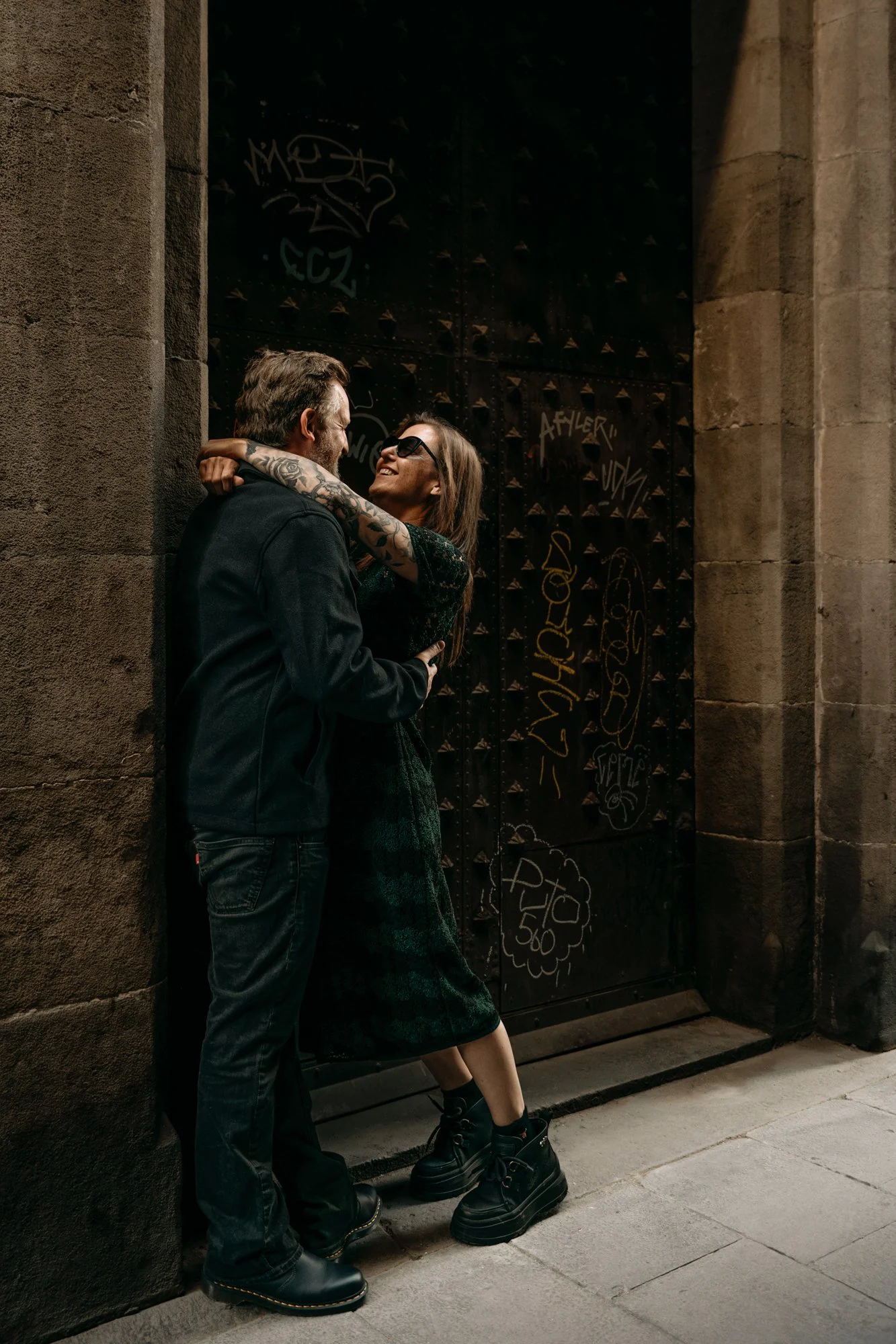 Couple embracing and smiling by a stone gate in Barcelona — portrait session by Whip & Honey