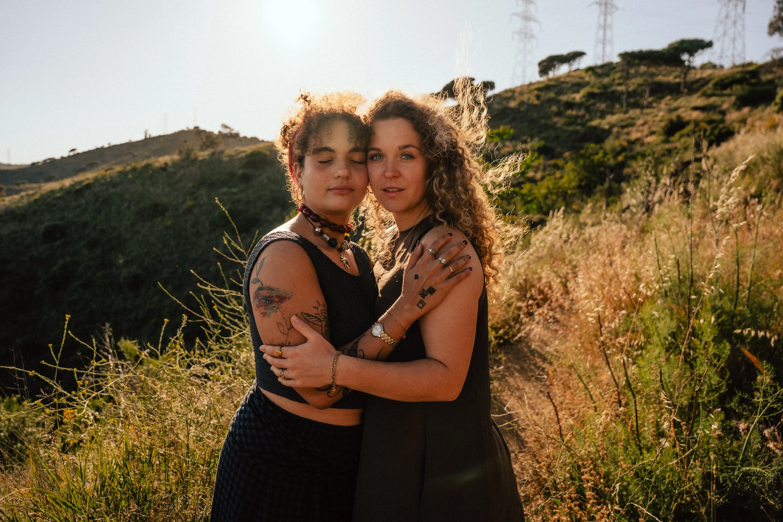 Two women hugging at sunset with Barcelona hills in the background — couples portrait session by Whip & Honey
