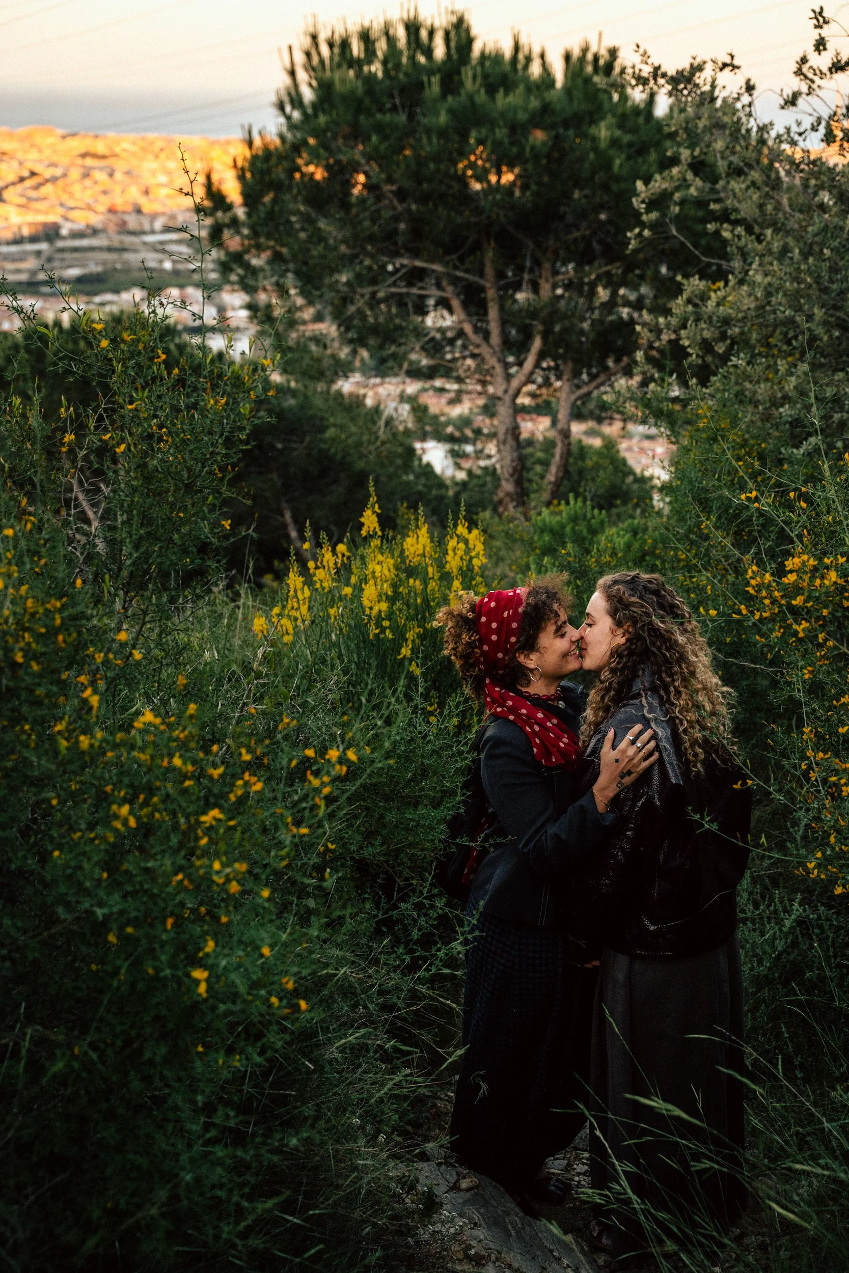 Two women kissing outdoors at sunset with Barcelona hills in the background — couples portrait session by Whip & Honey

