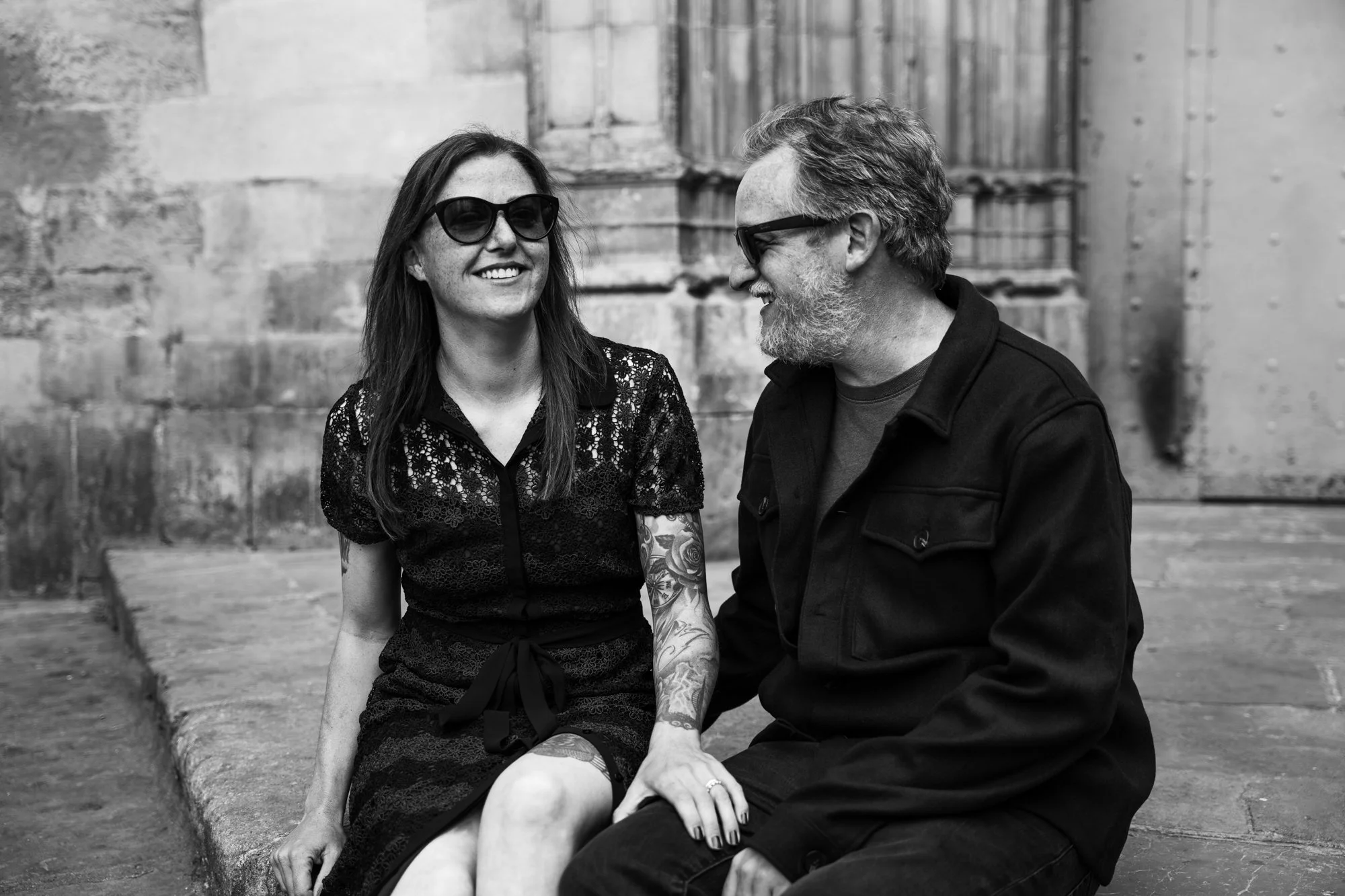 Couple sitting on a Barcelona curb holding hands and smiling — portrait session by Whip & Honey
