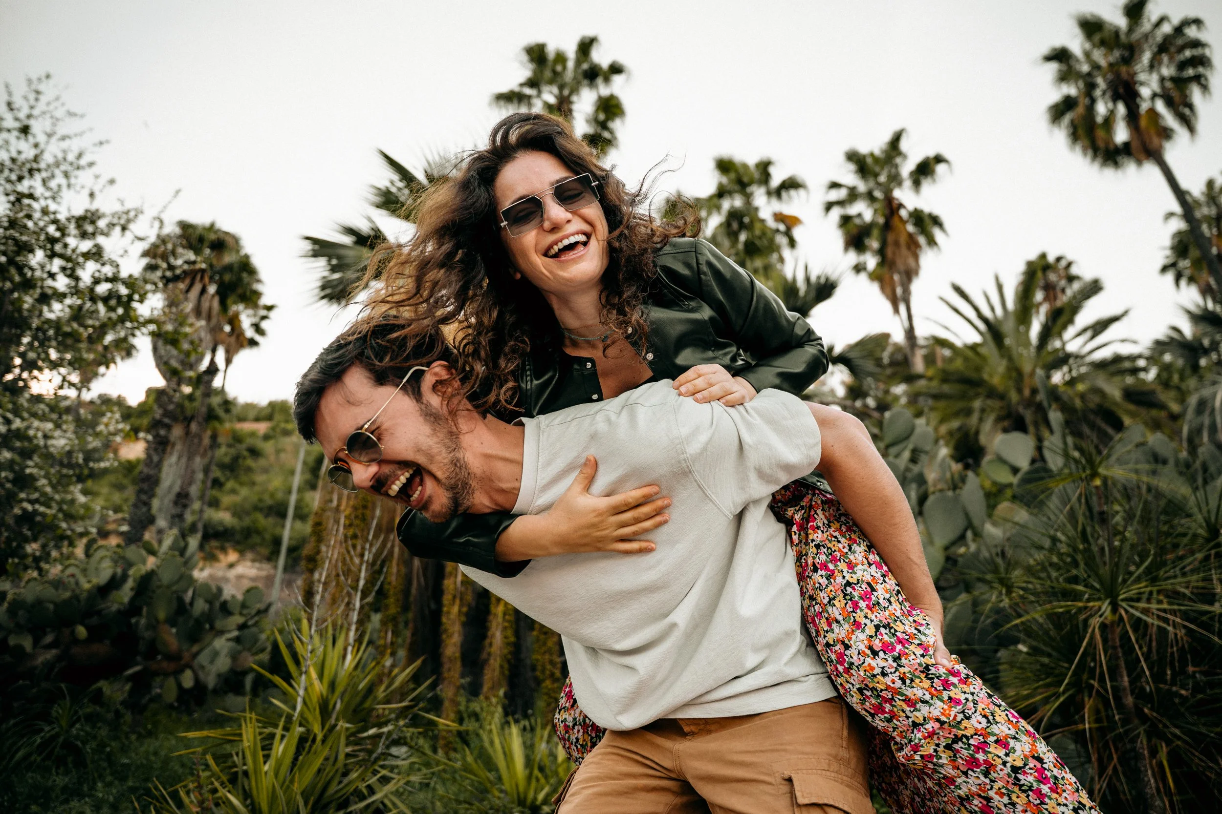 Couple laughing among palm trees in Barcelona, piggyback pose — couples portrait session by Whip & Honey
