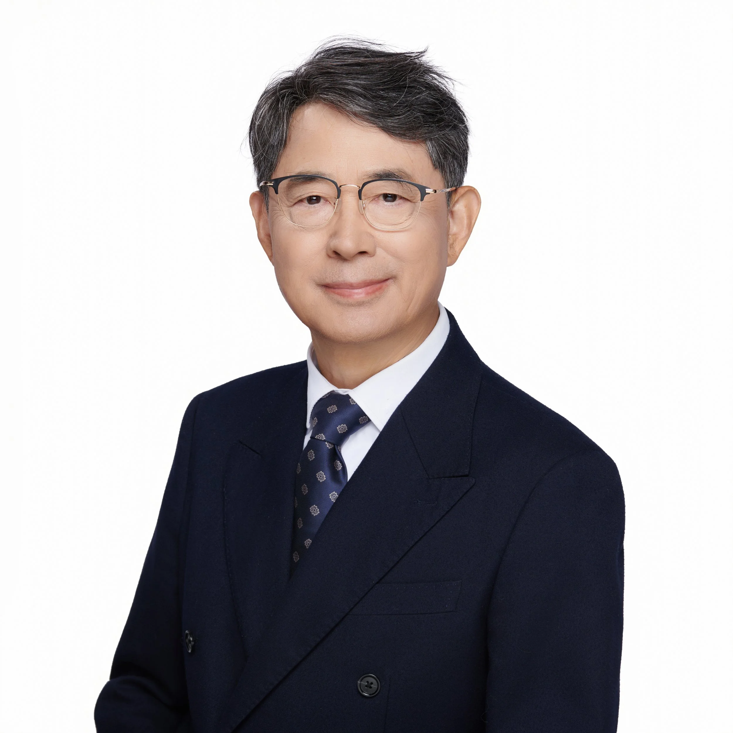 Headshot of a man with black and gray hair, wearing glasses and a dark suit with a tie, against a plain white background.