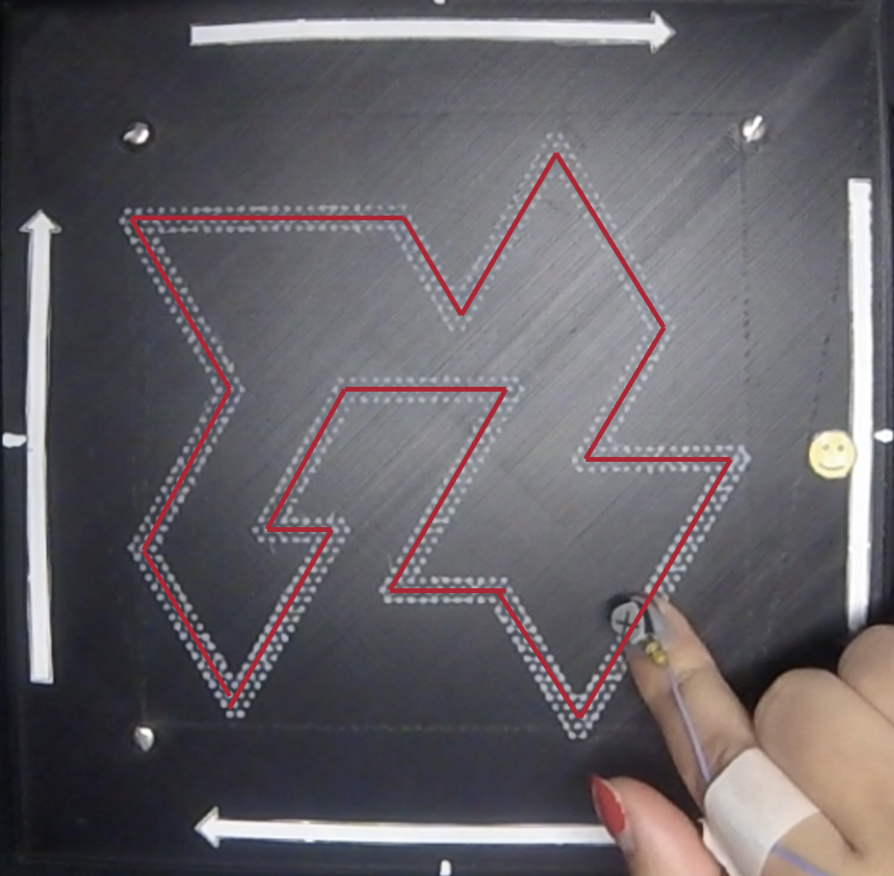 A black textured surface with white arrows on the top, bottom, and left sides, and a white arrow pointing right. Red outline trace on a white textured surface. Finger with a marker tracing the white surface.