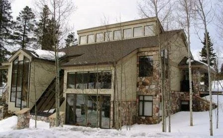 A multi-story house with a stone facade, large windows, and a snow-covered landscape.