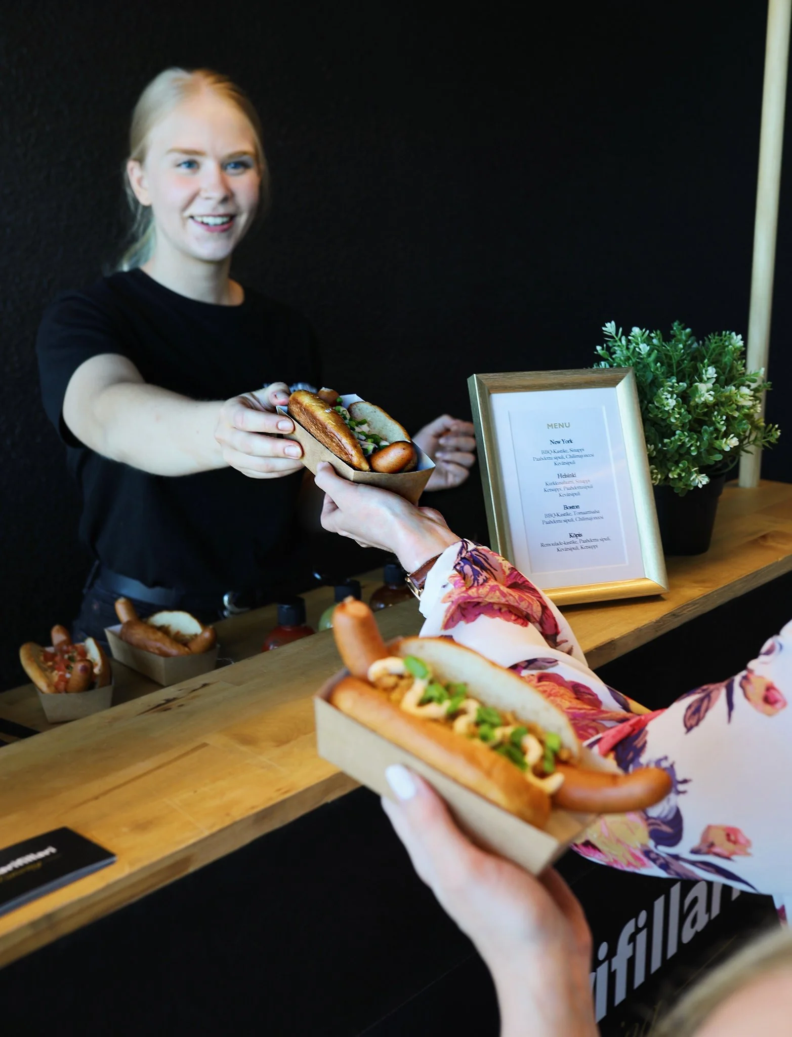 Nainen ojentaa toisen henkilön saadakseen Hodarifillarin premium hot dogin.