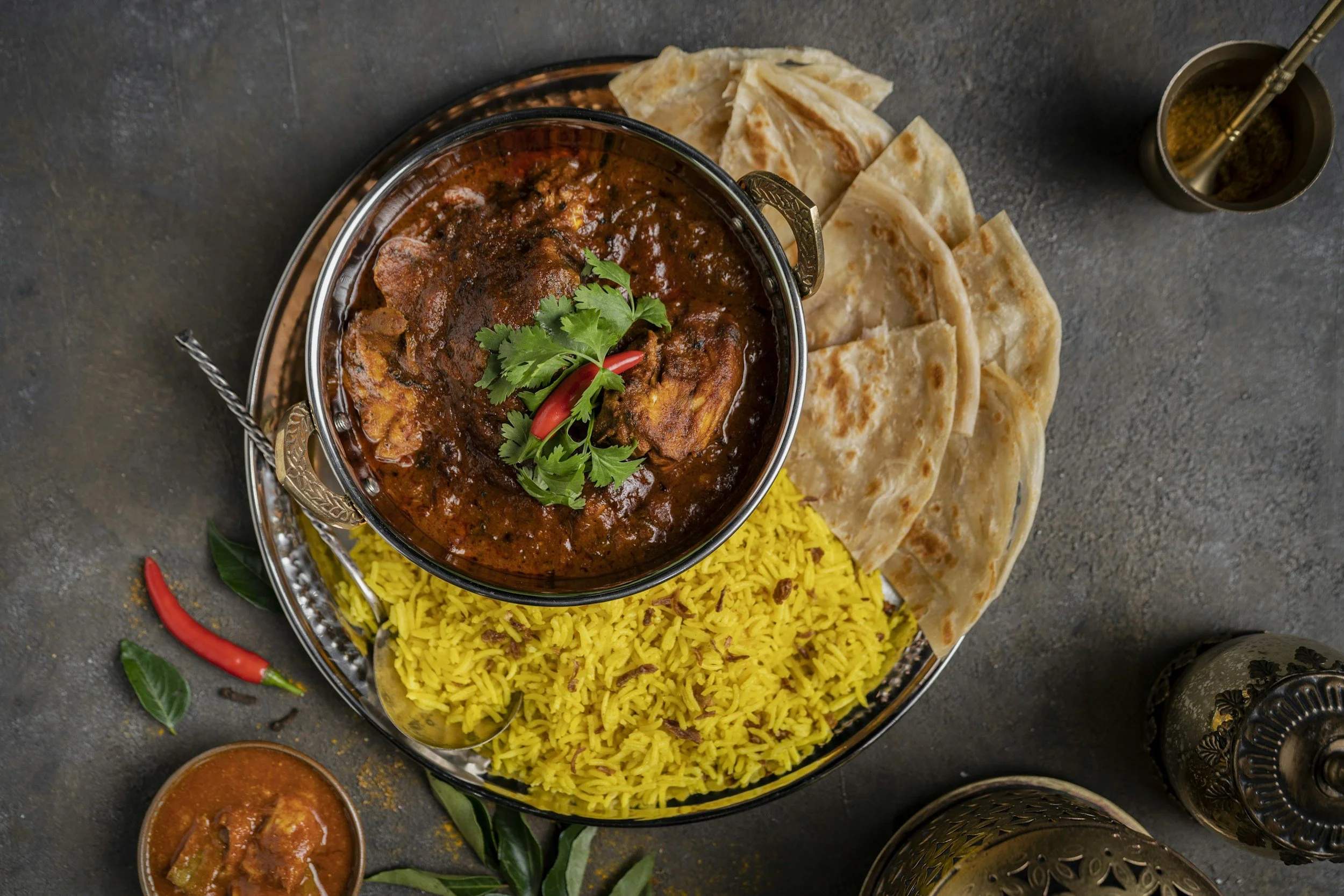A plate of Omani cuisine featuring yellow rice, bread, and a bowl of rich beef garnished with cilantro and chili peppers.