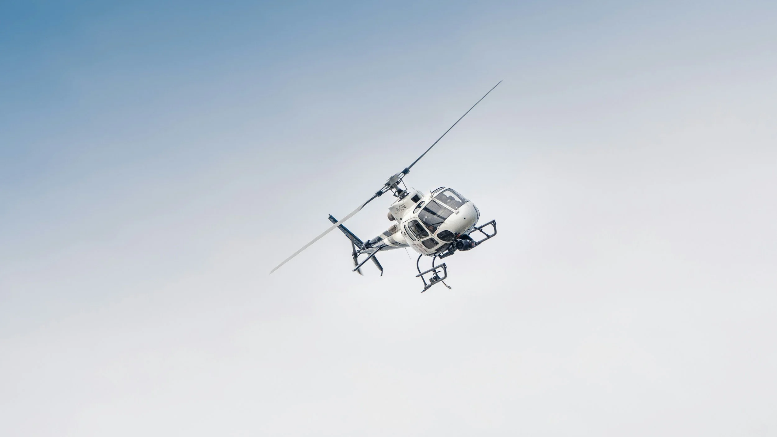 A white helicopter flying in a clear sky.