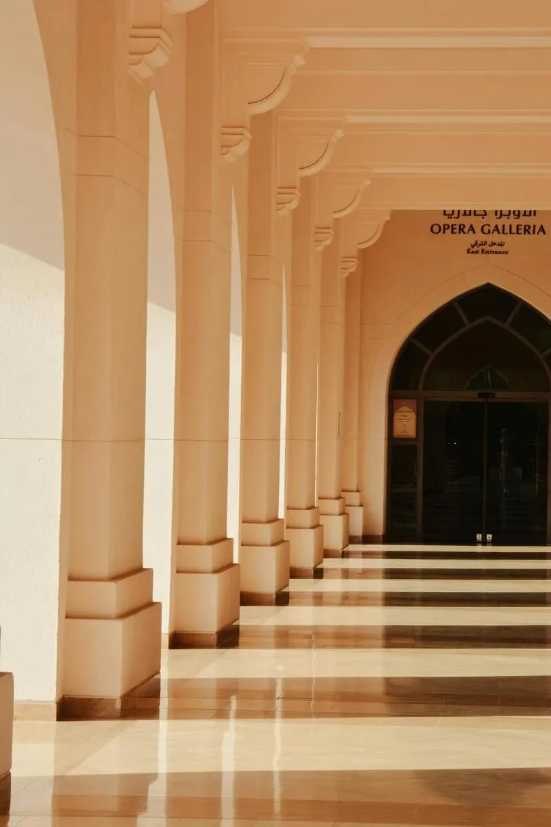 A hallway with cream-colored columns and arches, with a polished tiled floor and a sign indicating the east entrance of the opera gallery.