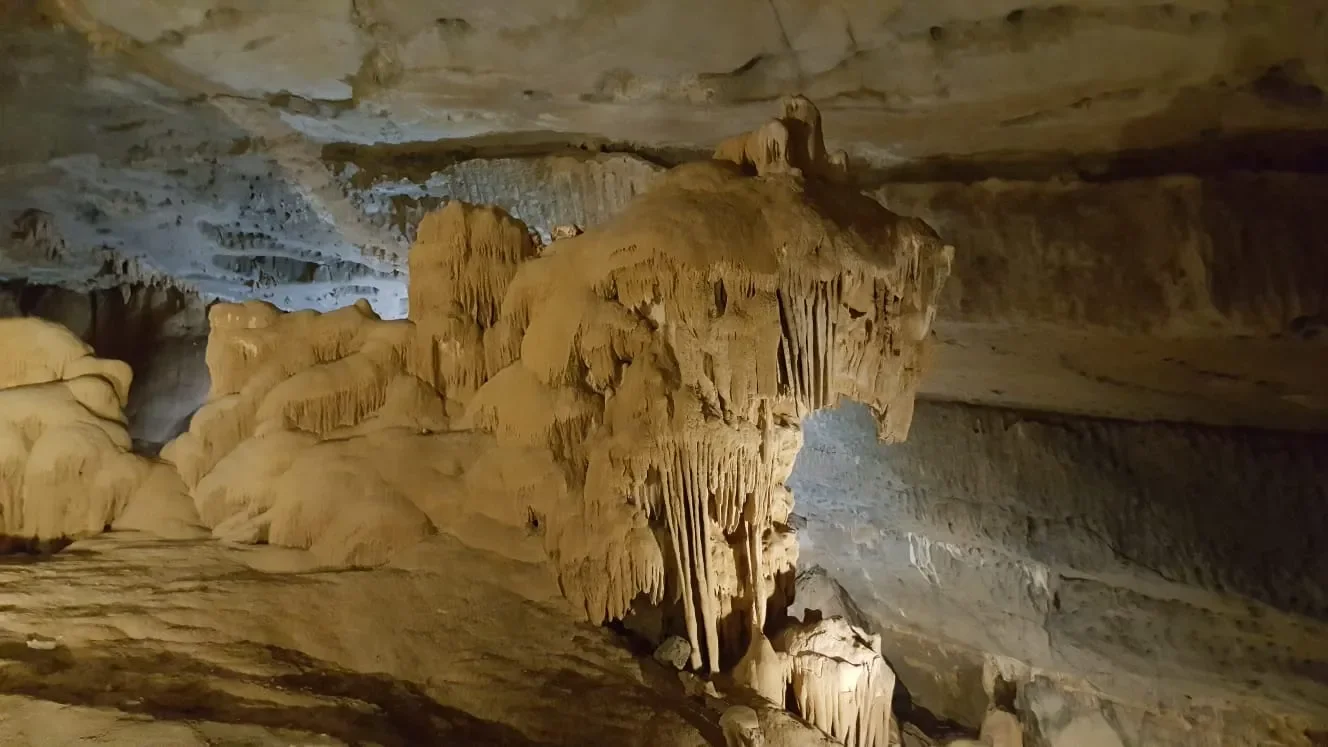 Inside a cave featuring stalactites and stalagmites formations, illuminated by soft lighting.