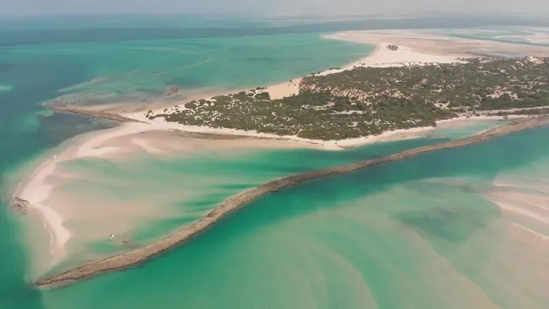 Aerial view of a coastal island with sandy beaches, green vegetation, and surrounding turquoise waters.