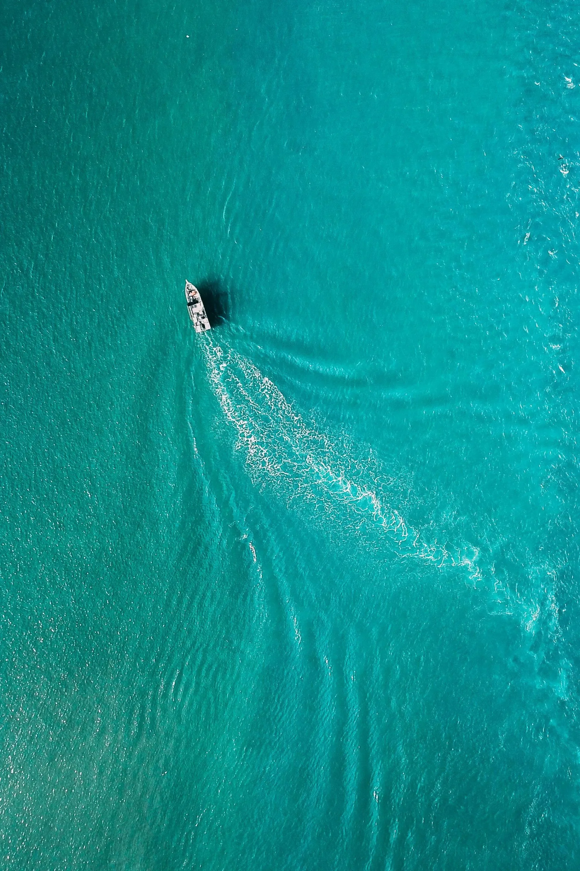 A boat sailing in clear turquoise waters, creating ripples behind it.