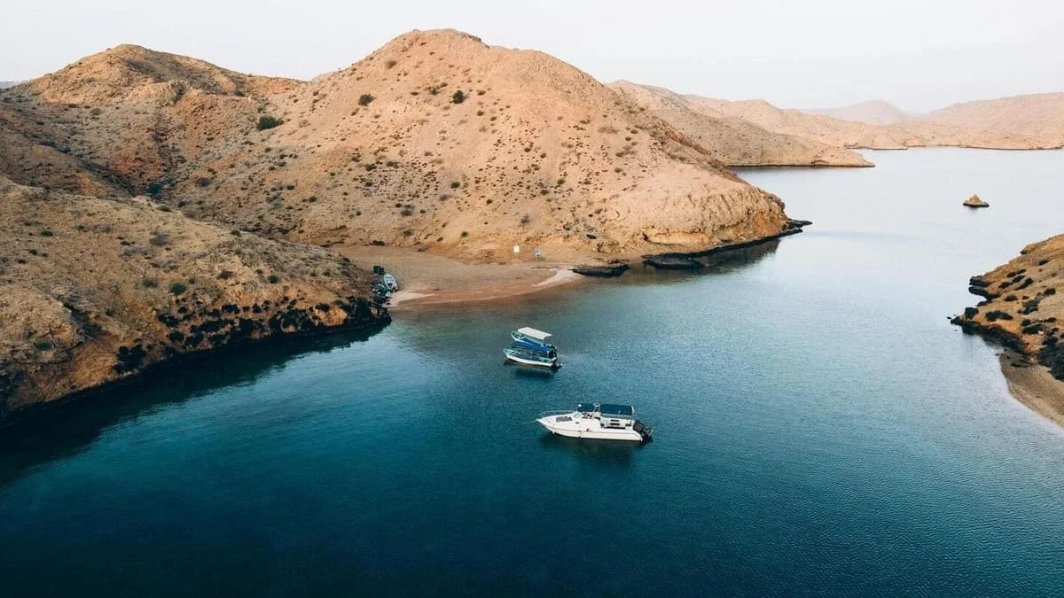 A serene body of water surrounded by arid, rugged hills with a few boats docked near the shoreline.