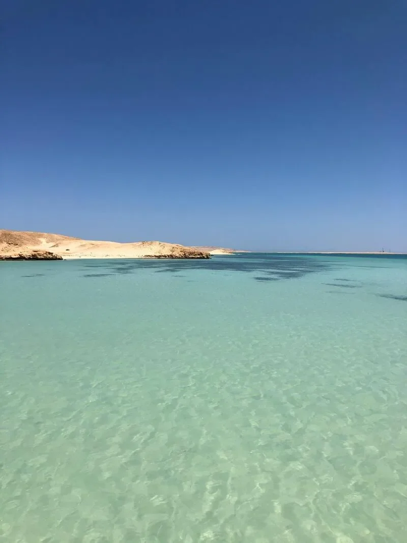 Clear turquoise water with distant sandy land and a blue sky.