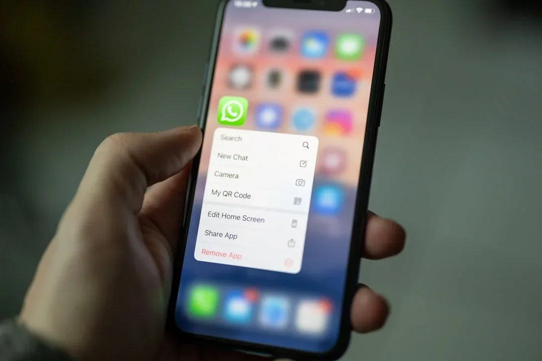 A person holding a smartphone with the WhatsApp app menu open on the screen.