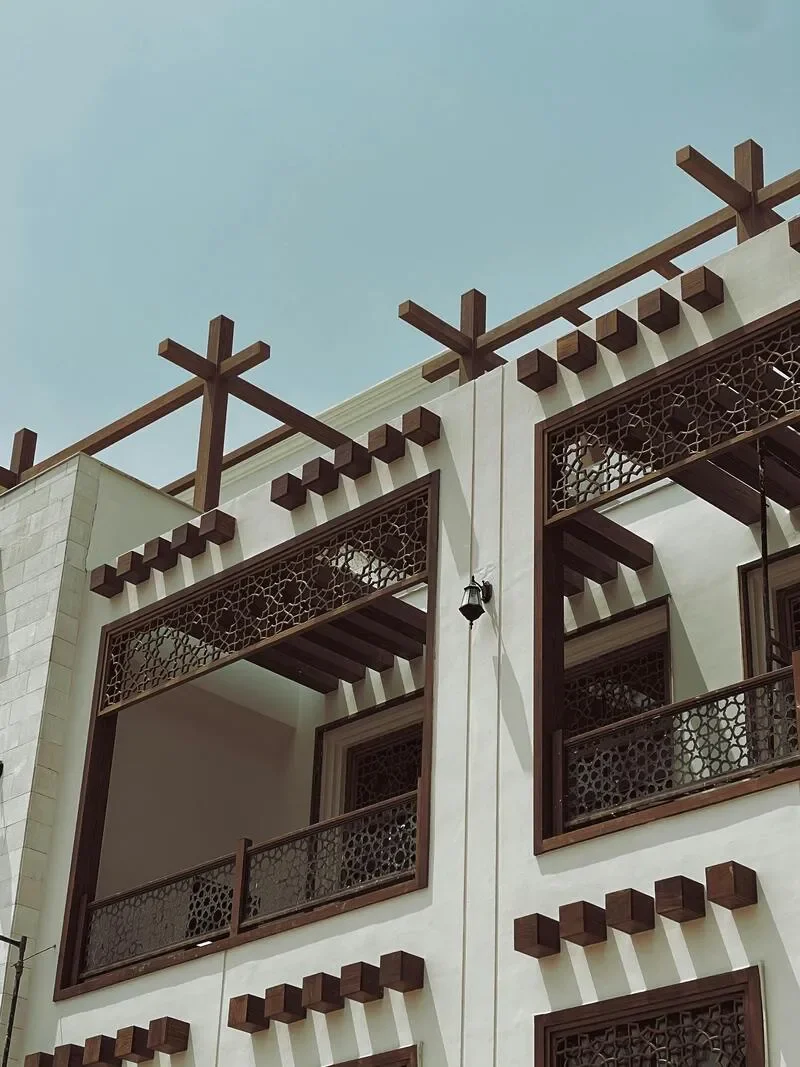A multi-story building with ornate wooden balconies and decorative lattice windows, featuring cross-shaped wooden beams on the rooftop against a pale sky.
