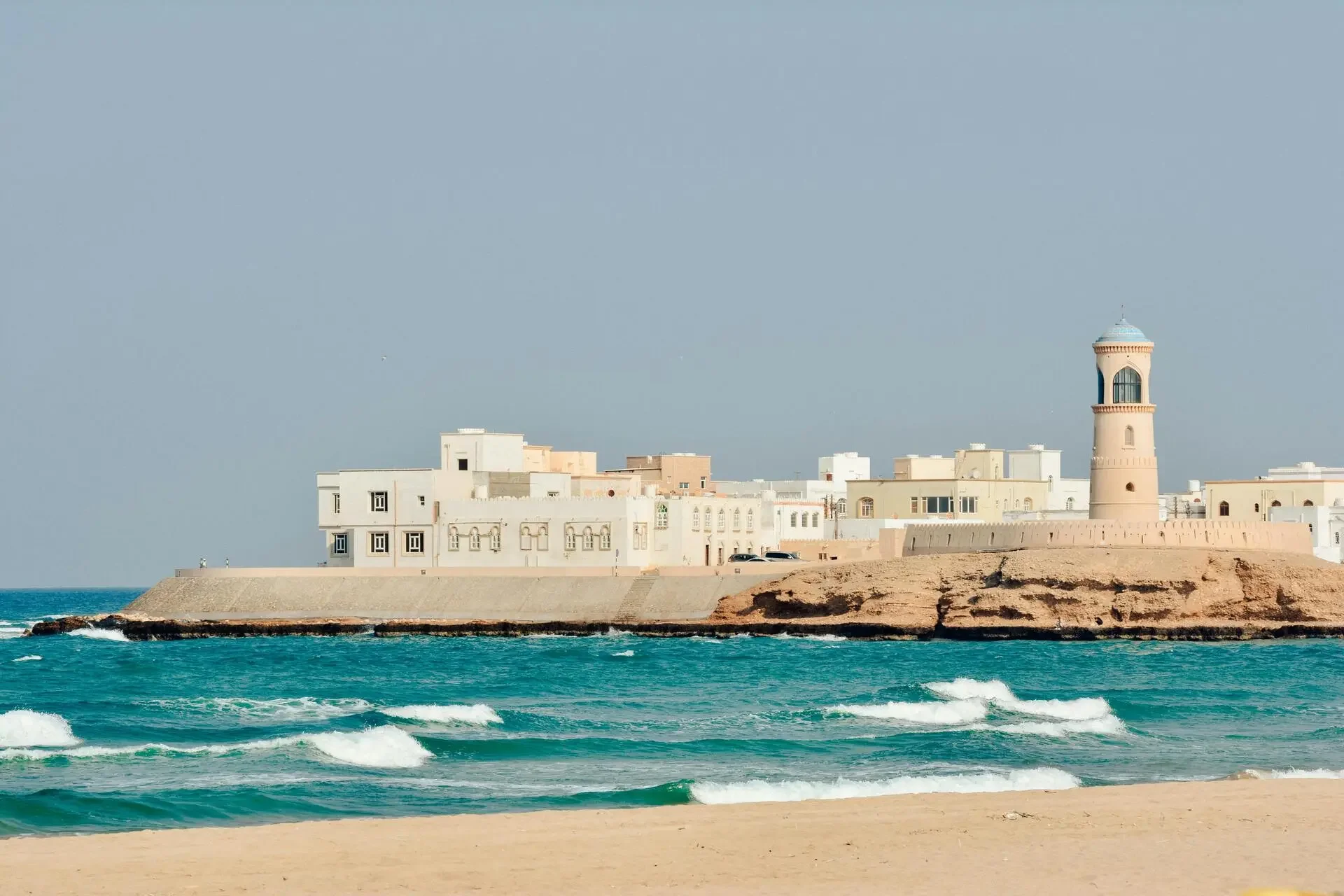 Coastal scene with buildings and a lighthouse along the shoreline under a clear sky.