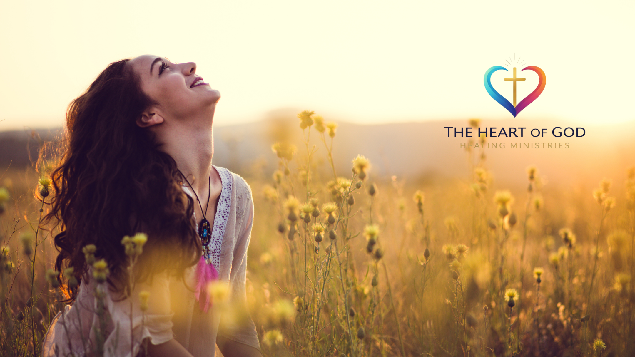 A woman with long, curly hair standing in a field of yellow flowers at sunset, looking upward with a joyful expression, with a logo for "The Heart of God Healing Ministries" in the upper right corner.