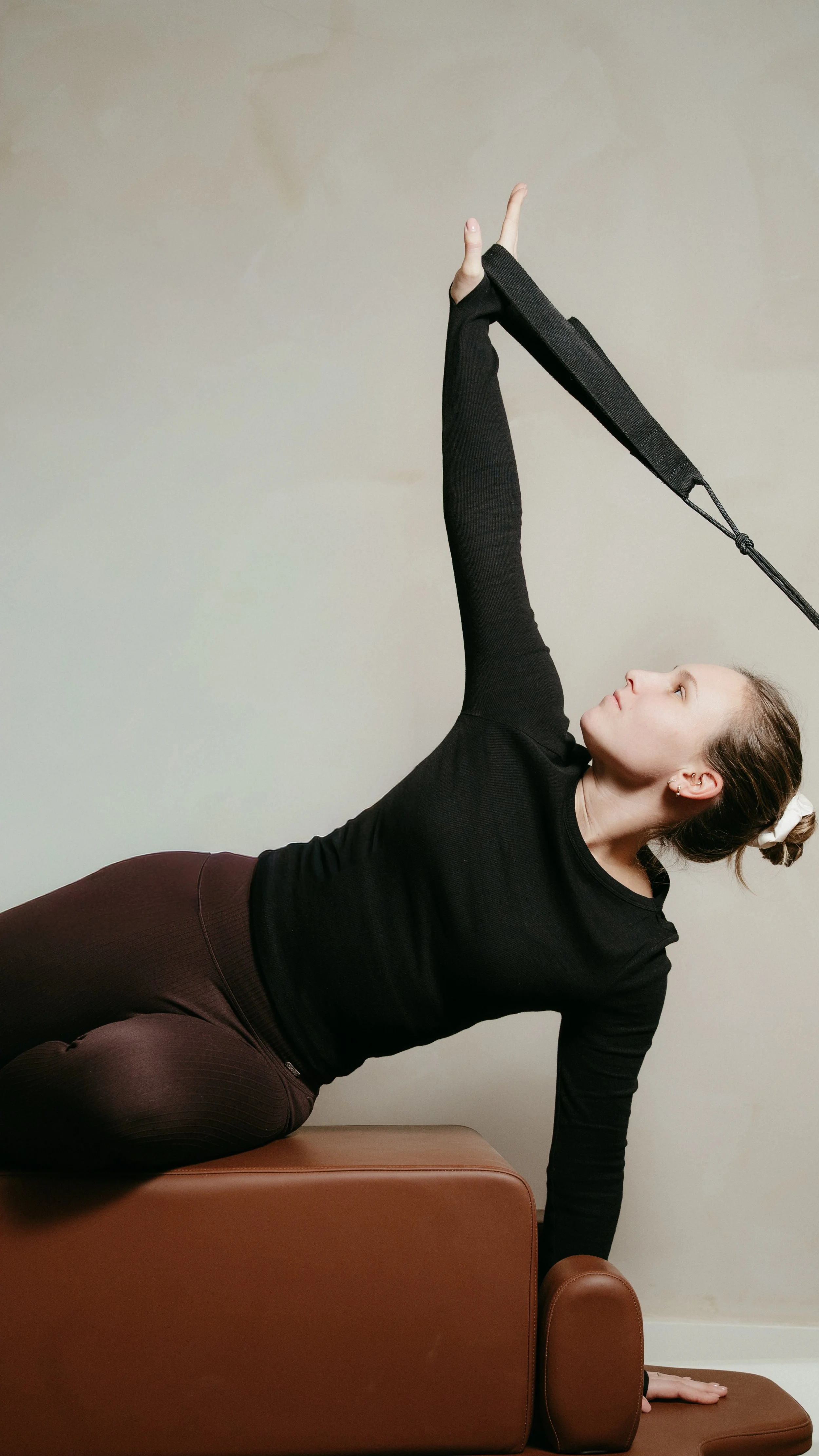 Een vrouw doet een yoga- of stretchoefening, liggend op een bankje, met haar rechterarm omhoog en haar hoofd omhoog gericht.