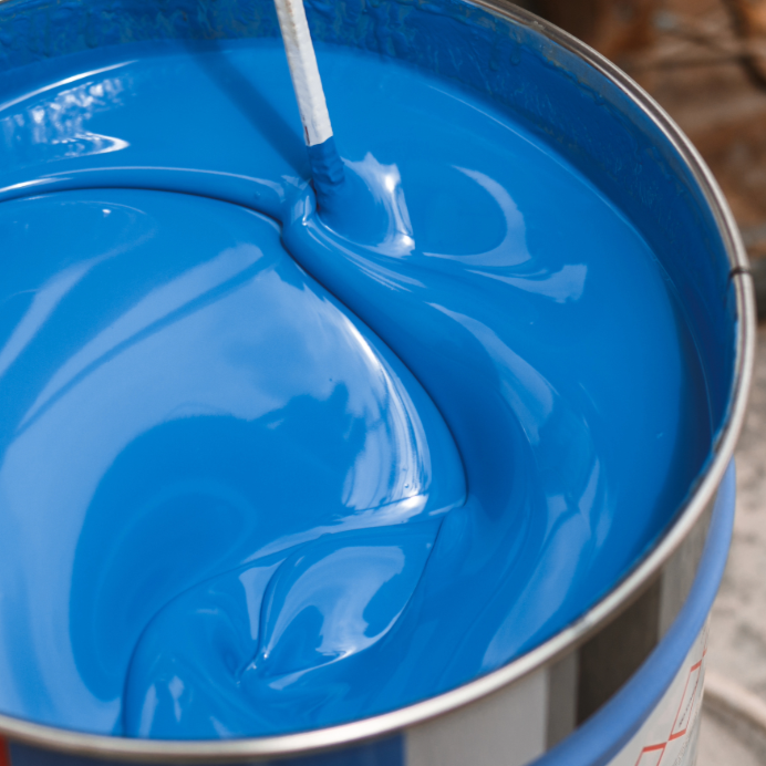 A metal bucket filled with bright blue paint and a stir stick inside.