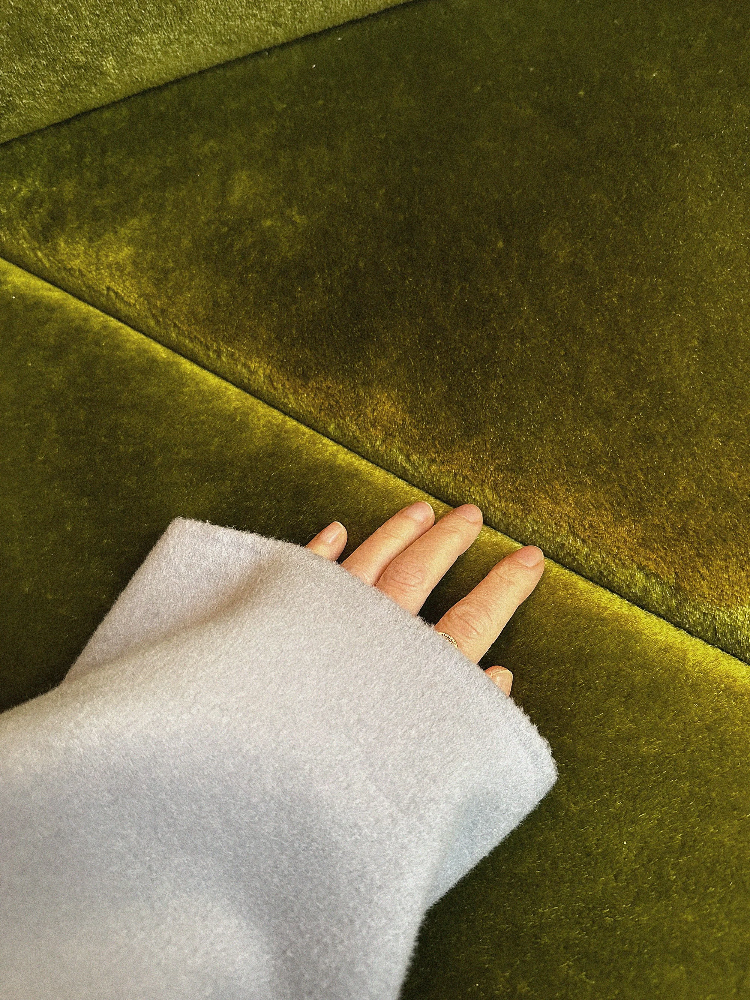 Close-up einer Hand auf goldgrünem Samtstoff in babyblauer Wolljacke.