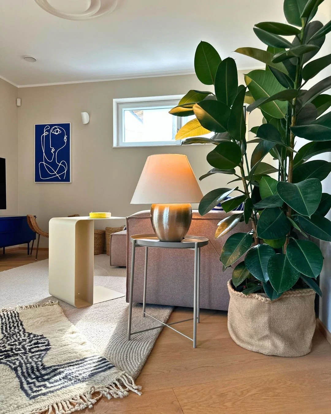 Wohnzimmerdesign mit hellem Holzboden, große grüne Topfpflanze, Naturmaterialien, Geometrie, taupefarbenes Sofa, gelber Metalltisch, marokkanischer Teppich