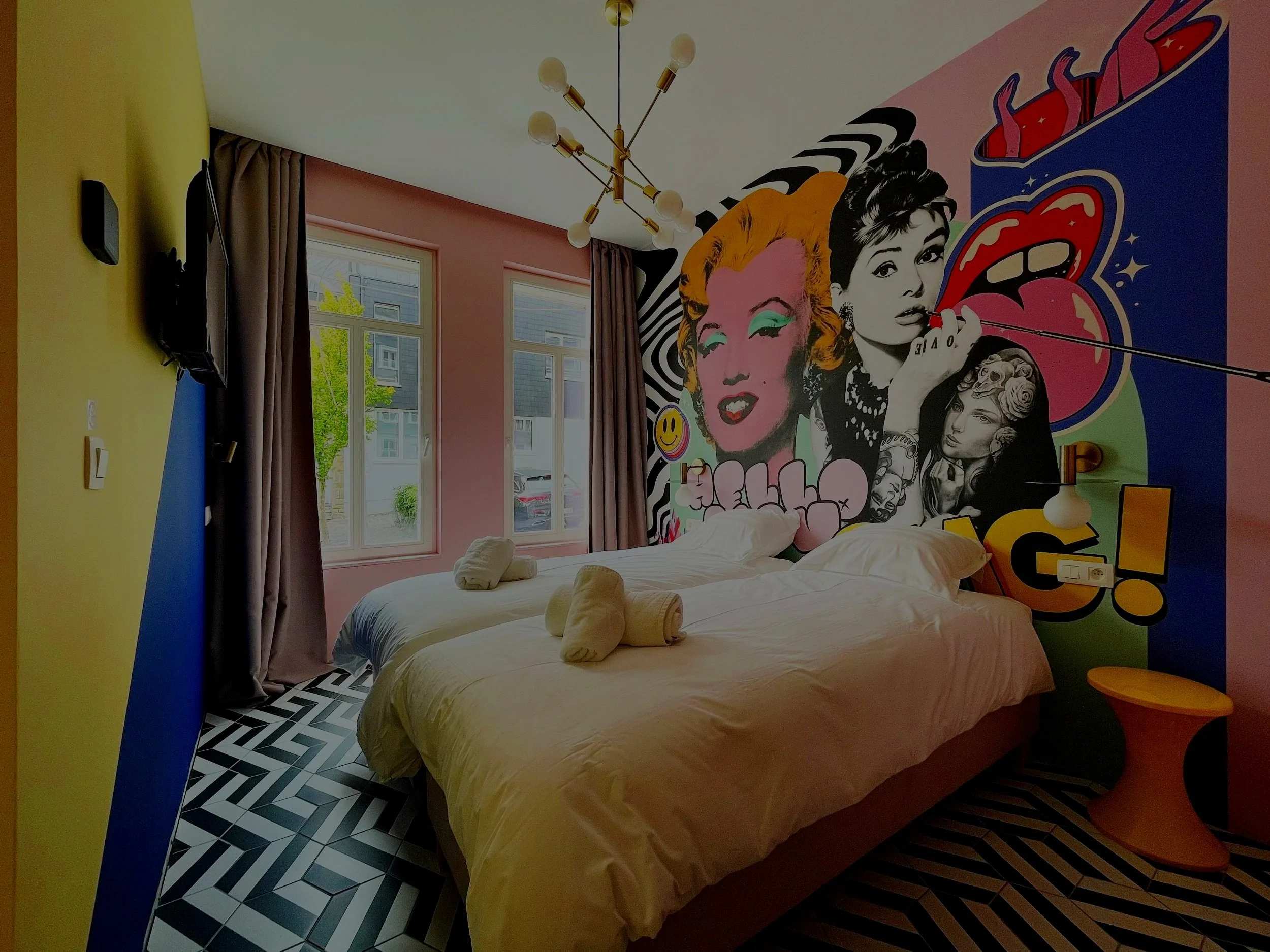 Chambre colorée avec mur en graffiti artistique de deux femmes, fenêtres, et meubles modernes, style pop art.