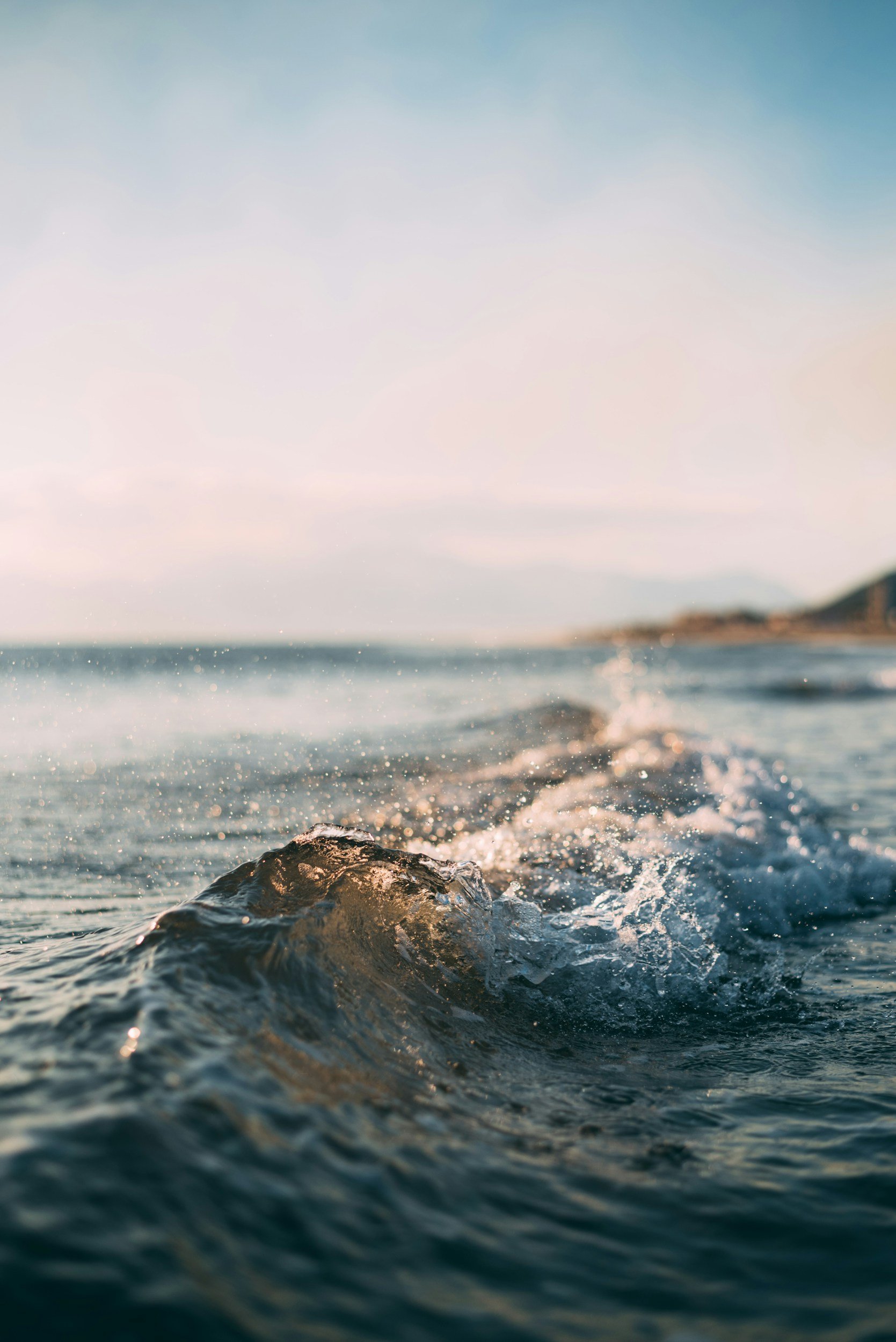 Close-up of ocean waves with a blurred coastline in the background and a clear sky above.