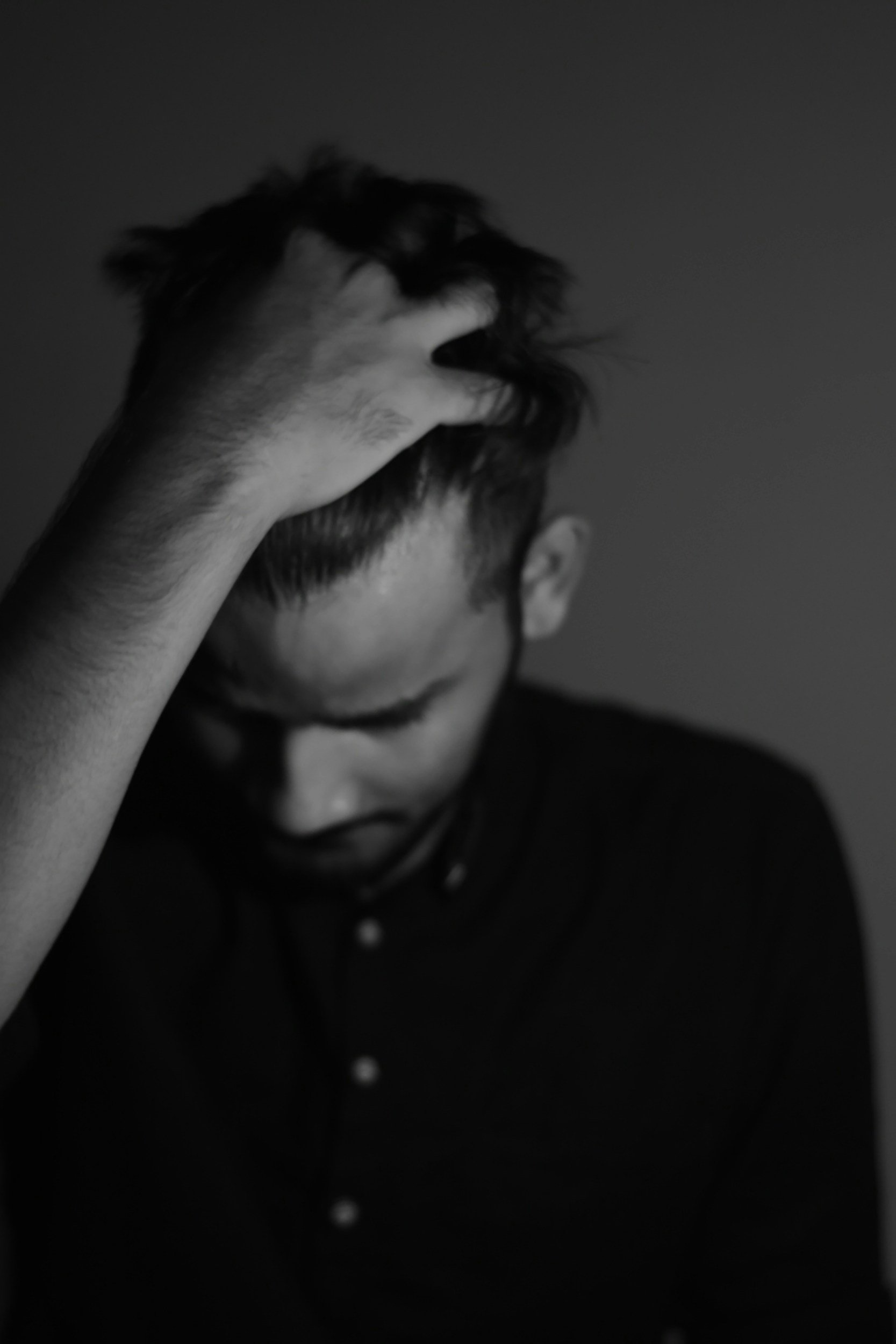 A person with short hair is holding their head with one hand, looking down, in a black and white photograph.