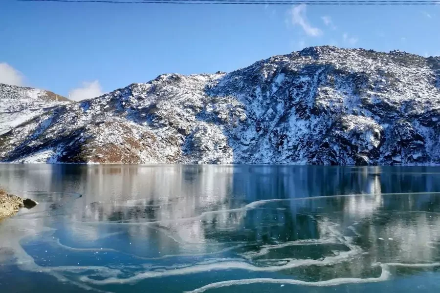 Snow-covered mountain behind a frozen lake with ice patterns on the surface.