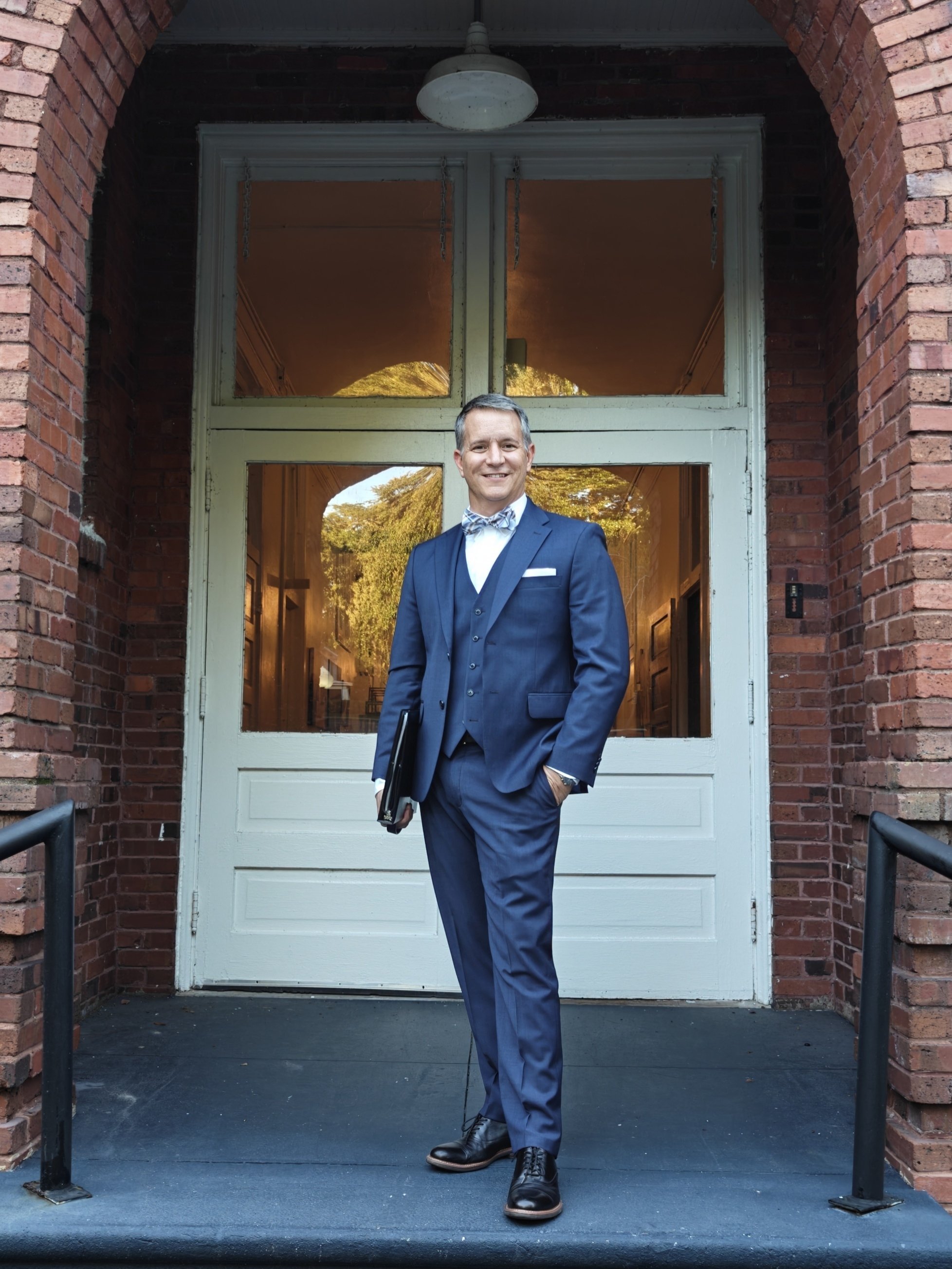 Guy Swenson holding a portfolio in a blue suit representing executive digital narrative strategy for educational leaders