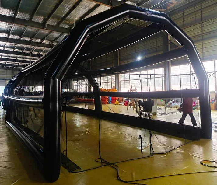 A large indoor inflatable soccer field with black inflatable borders and netting, set up inside a spacious warehouse or sports facility.