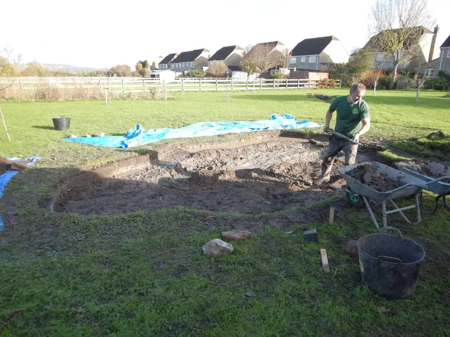 Person working on excavation in a backyard with houses in the background.