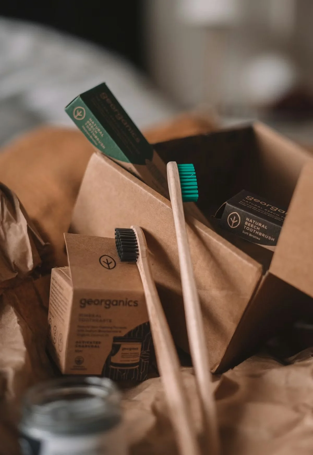 Various packaging for organic and natural personal care products, including toothbrushes and toothpaste, inside a cardboard box.