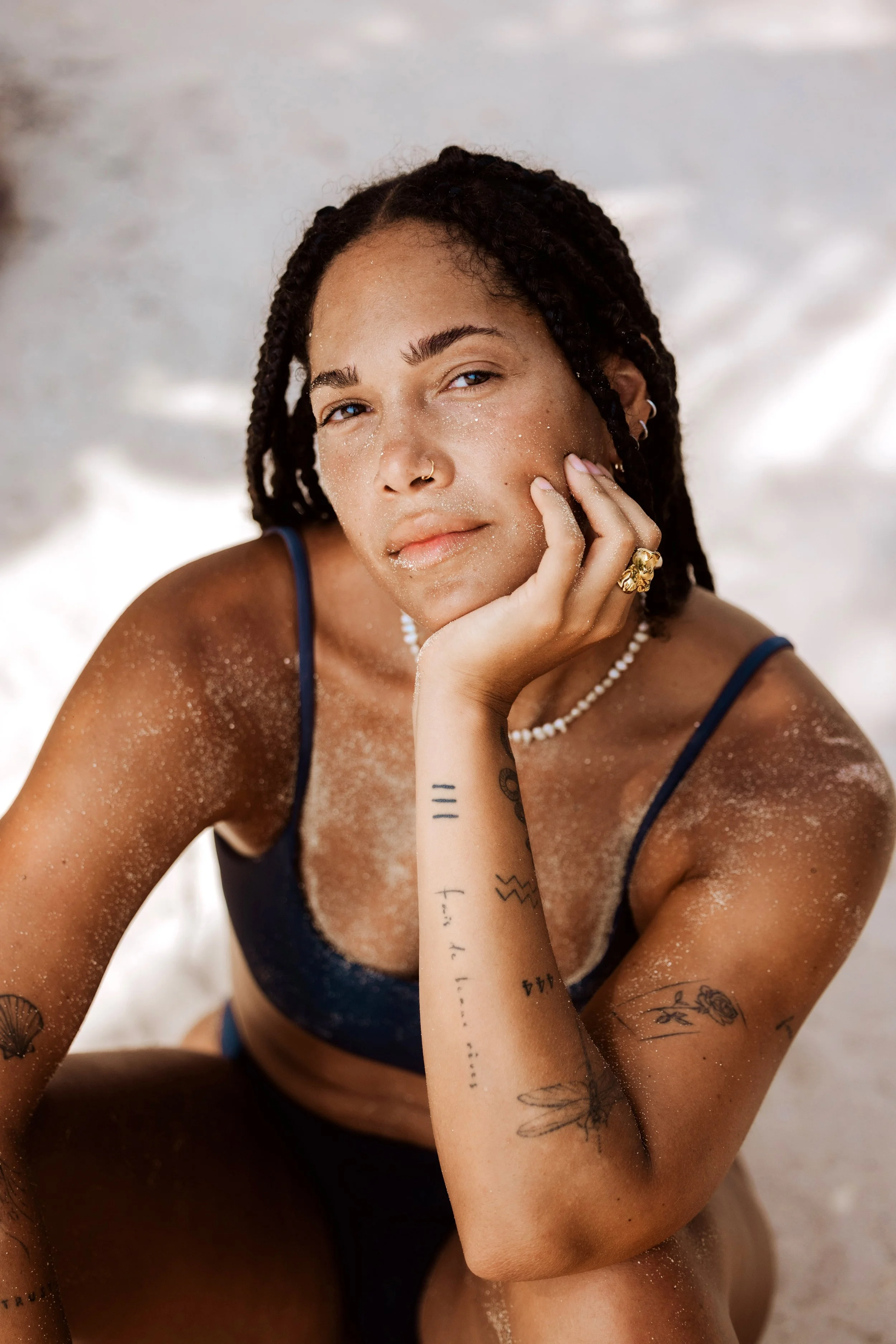 Person with braided hair, sandy skin, and tattoos in swimwear.