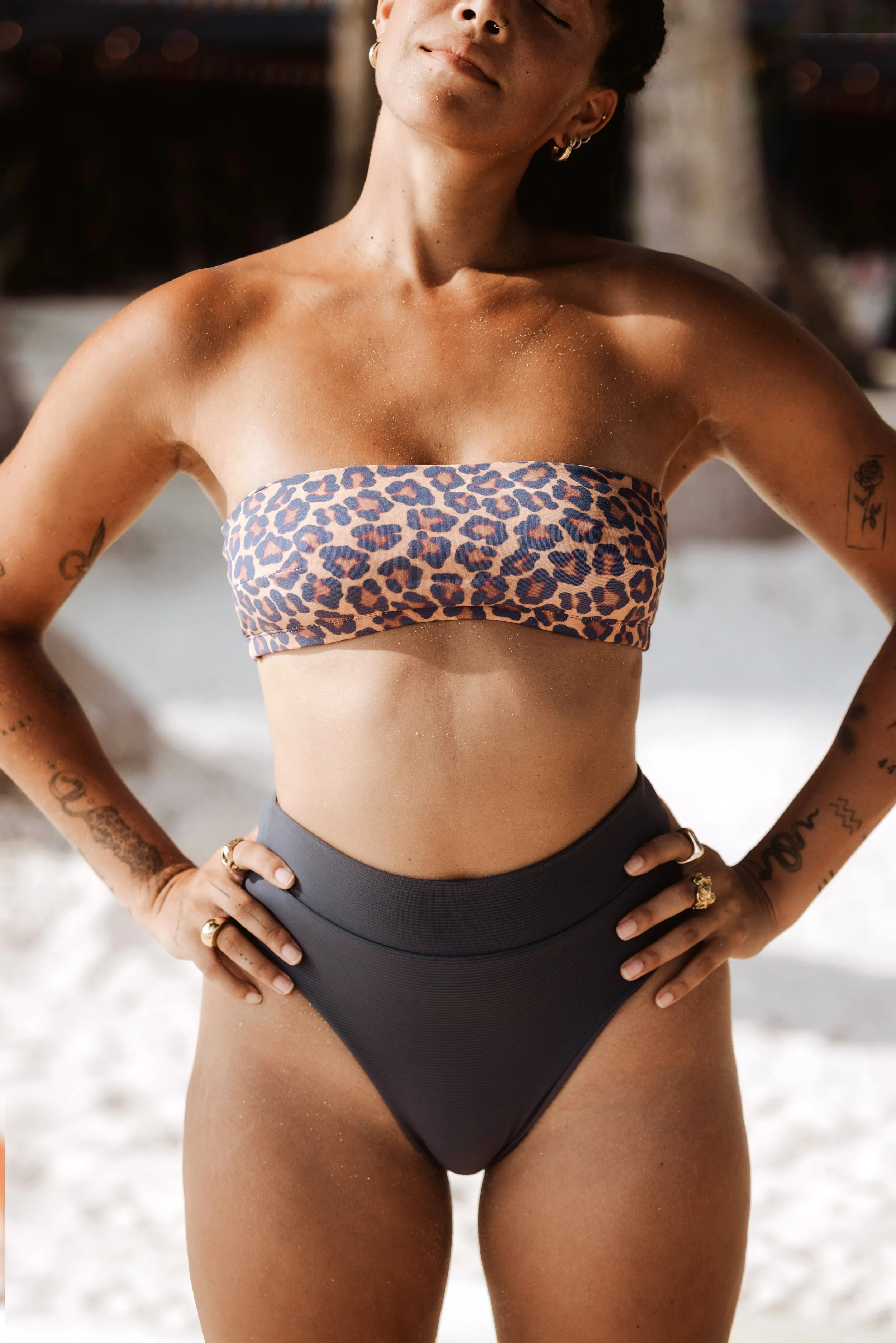 Person wearing a leopard print bandeau bikini top and dark high-waisted bottoms on a beach.
