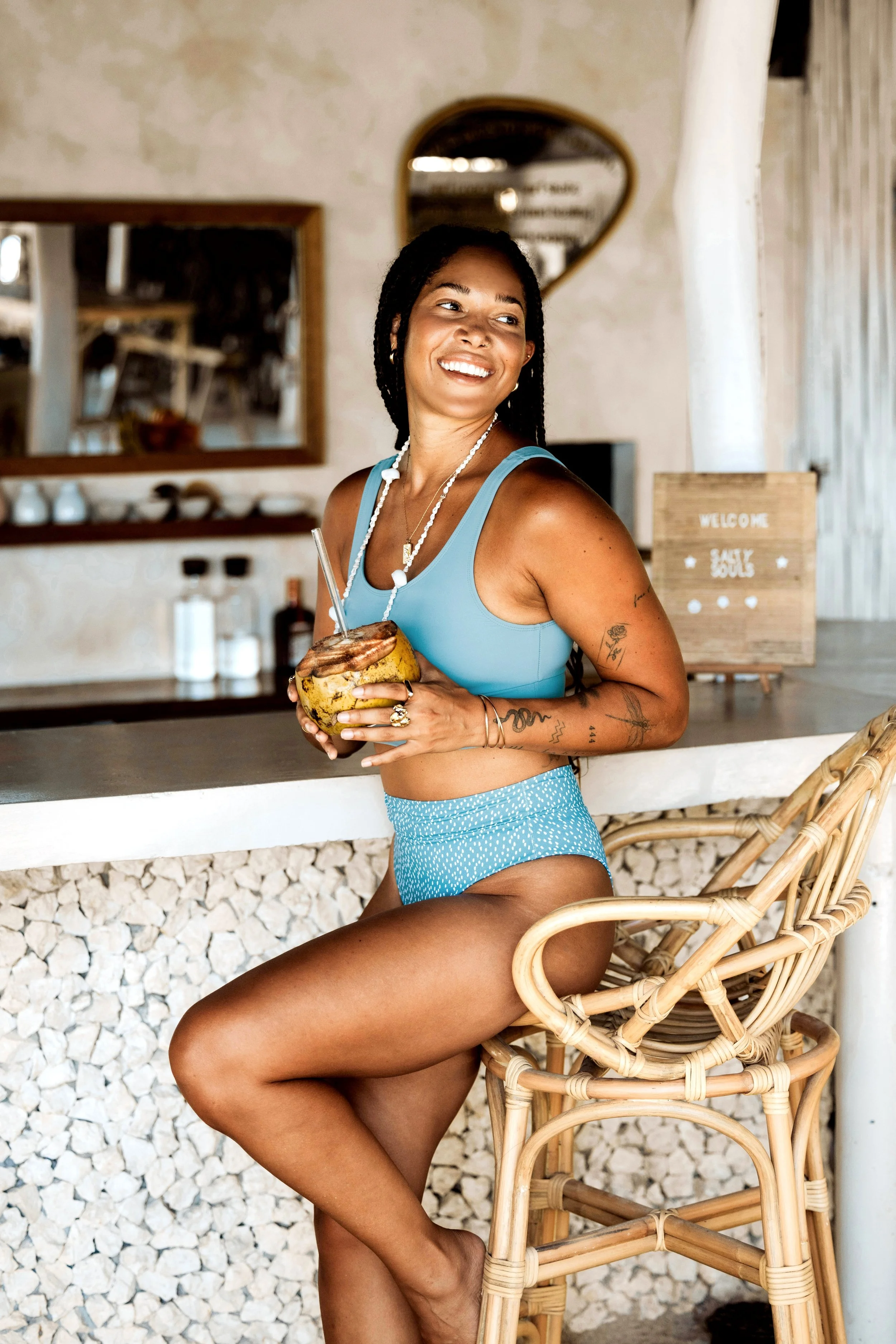 Woman in blue swimsuit sitting at a tropical-themed bar with a coconut drink.