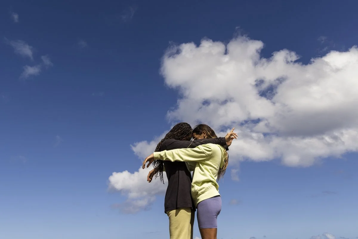 Two people embracing under a blue sky with clouds.